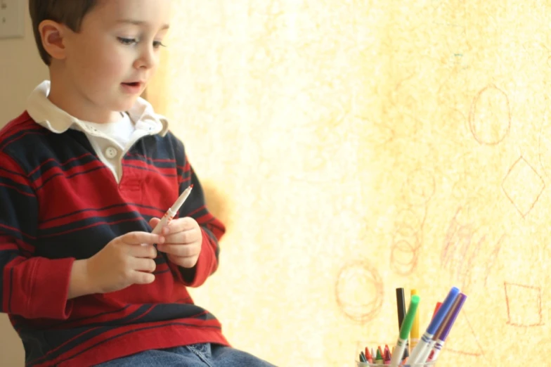 a boy in a striped shirt is holding some pens