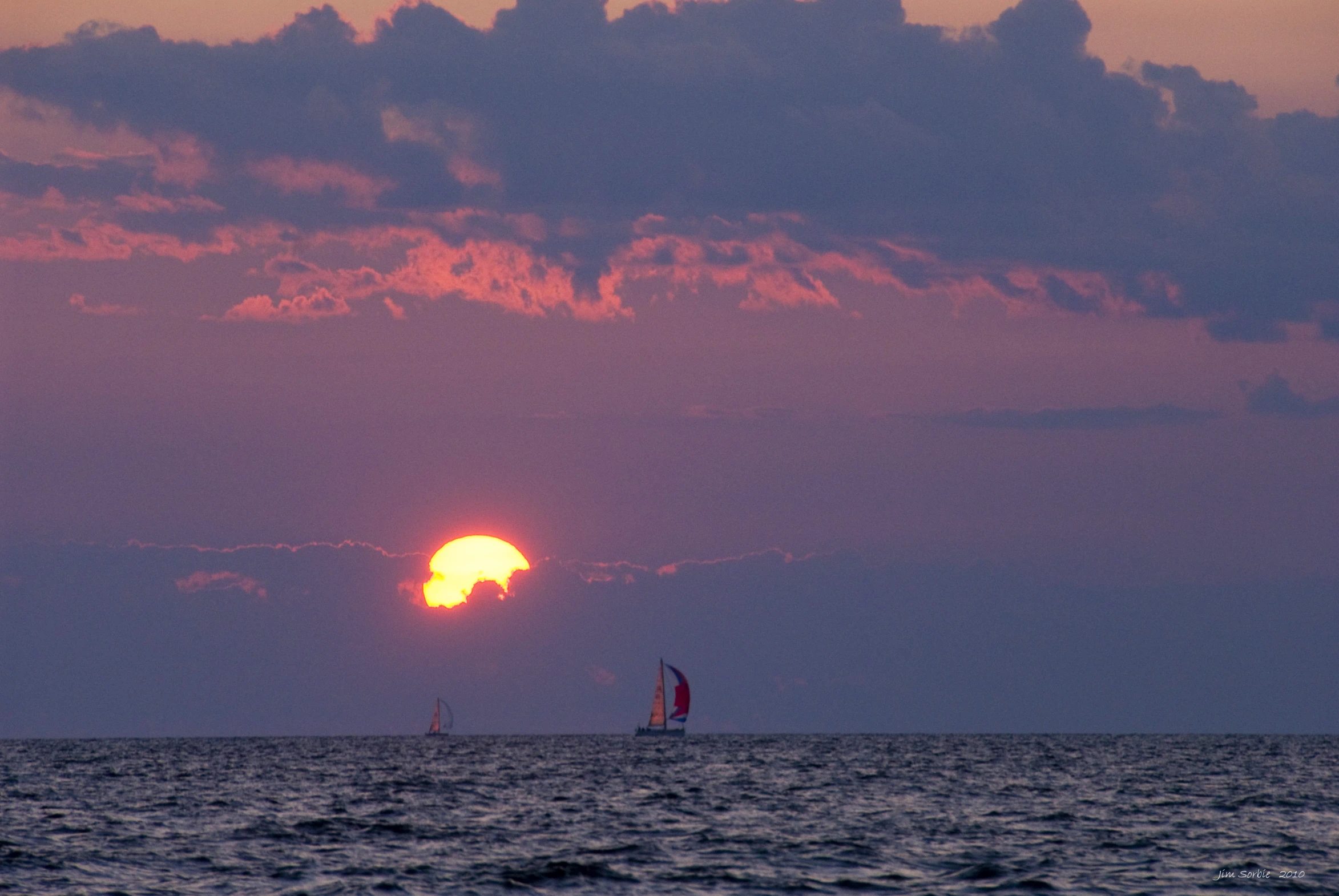 the sun is setting behind a sailing ship in the water