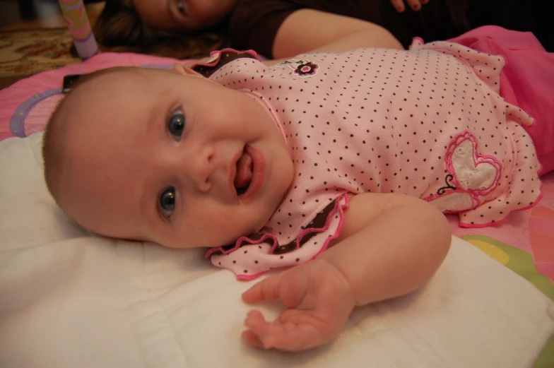 a baby lays on her stomach while looking at the camera