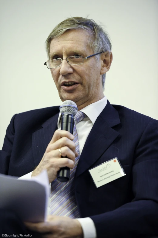 man with glasses holding microphone in front of a speaker