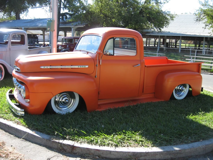 an orange truck parked in a grass yard next to a white car