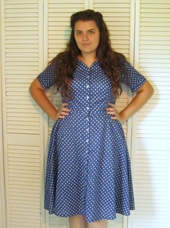 a woman in blue and white dress standing by a white wall