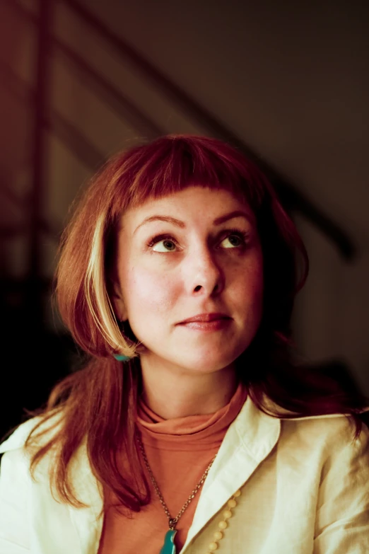 woman with red hair and large necklace sitting in front of stairs