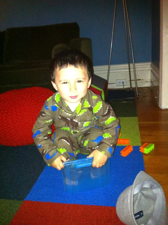 a boy sitting on the floor with a plastic container