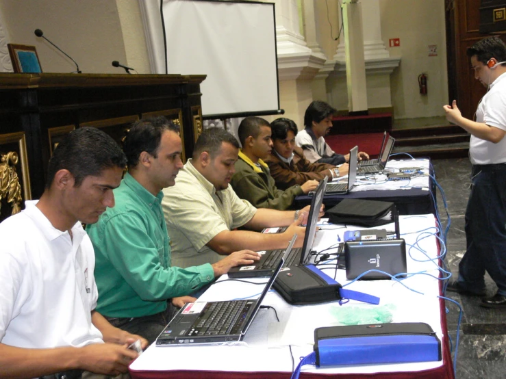 a group of people using laptops with an official man looking on