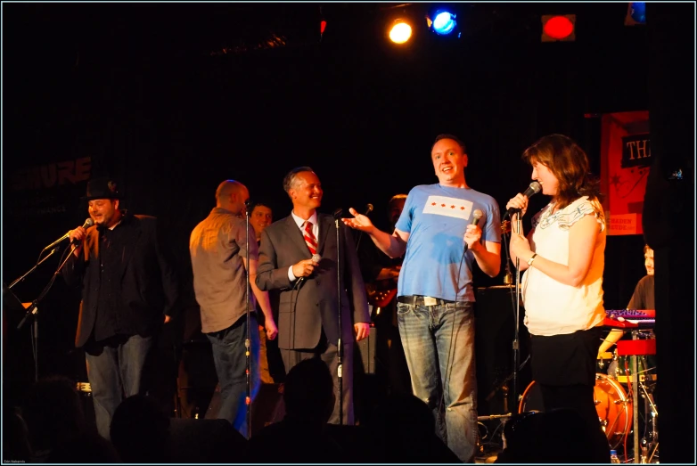 a group of people stand on a stage while one person holds a microphone