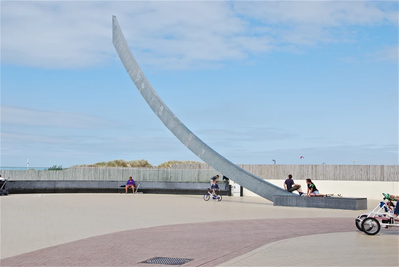 children skateboard and bike past a large sculpture