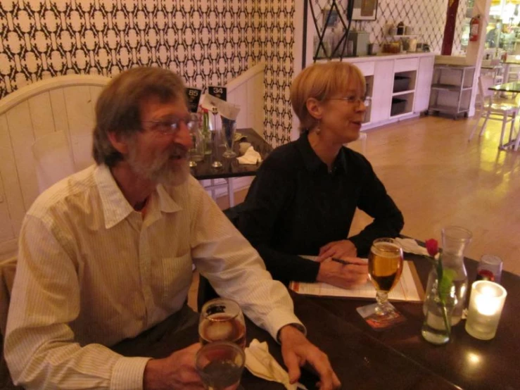 two men sitting at a table holding glasses in their hands