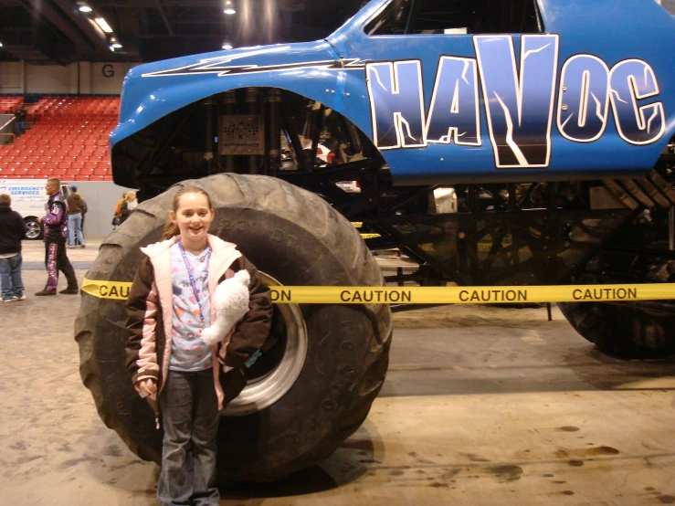 a child poses in front of monster truck at an indoor arena