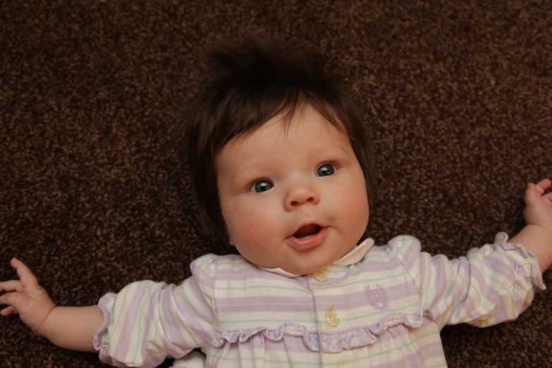 a baby with her arms up laying on the ground