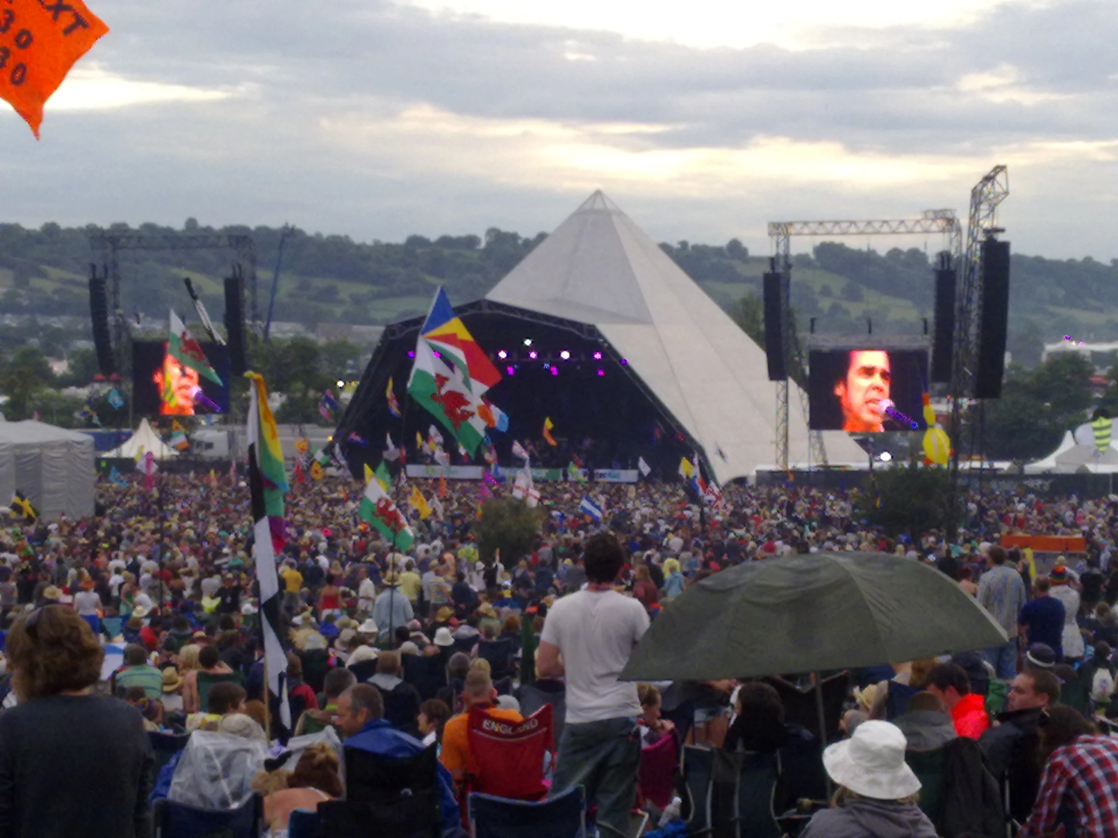 people at an outdoor concert with large screens and flags