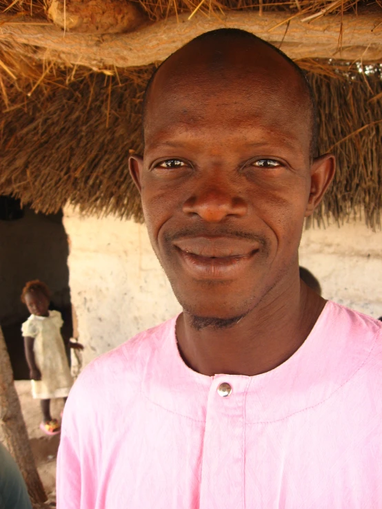 an african man smiles in front of a hut