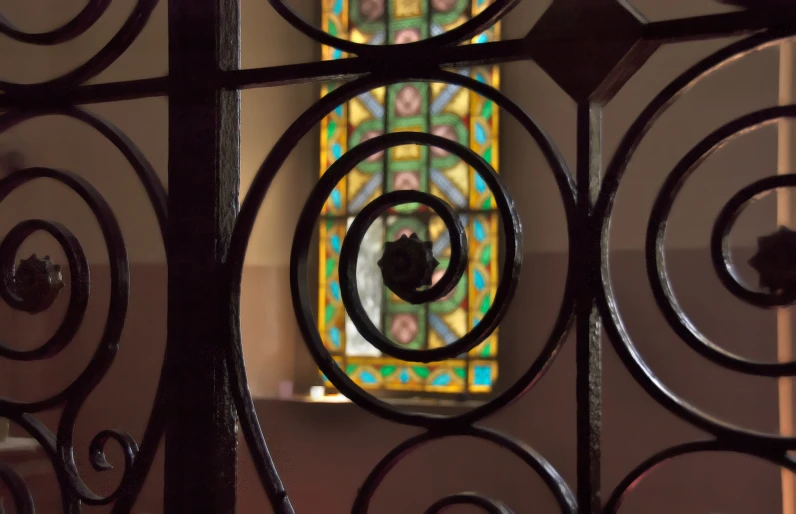 a closeup of an iron fence with a stained glass window in the background