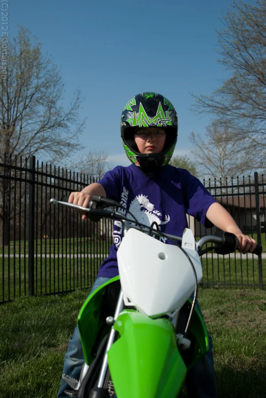 little boy in helmet on green motorcycle parked on grass