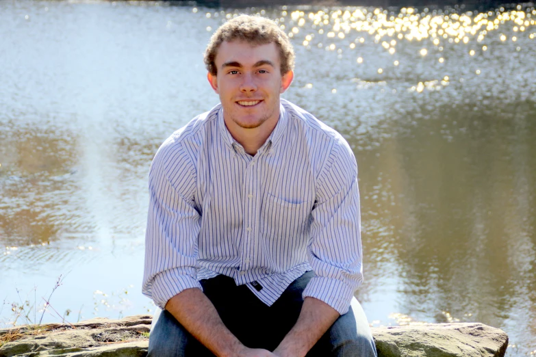 a man sitting on the edge of a cliff near water