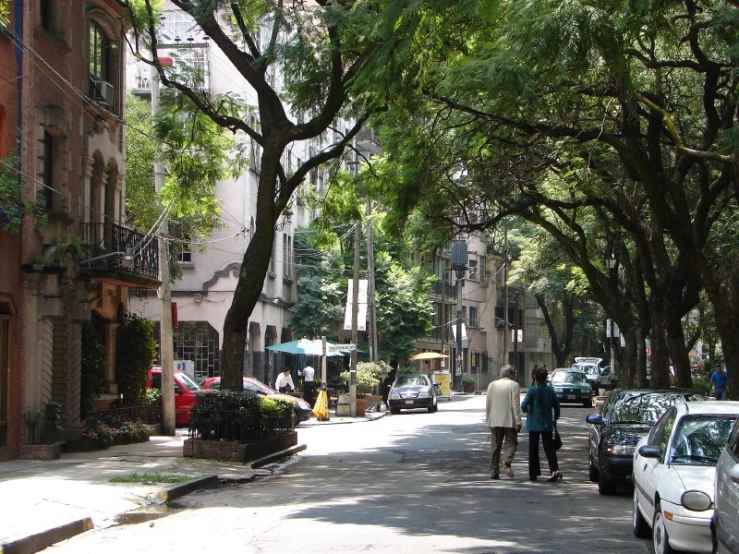 two people walking down a street by parked cars