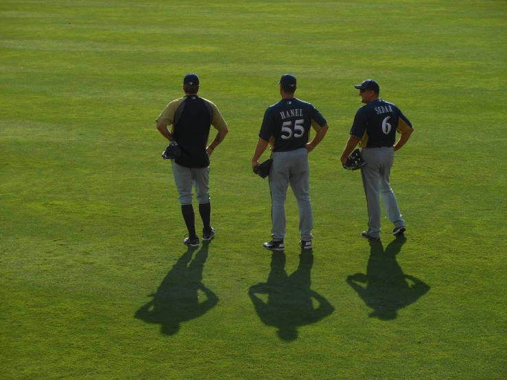 three men wearing baseball uniforms stand on grass