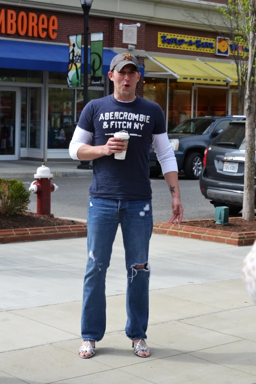 a man in jeans and a t - shirt holds up a  cup while standing outside