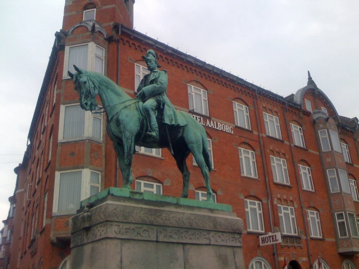 the tall brick building has a horse and rider statue in front