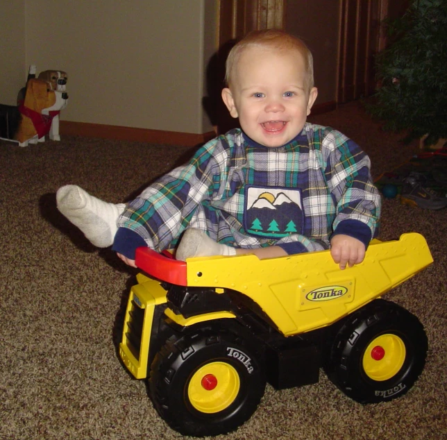 a baby in a blue shirt sitting on a toy truck