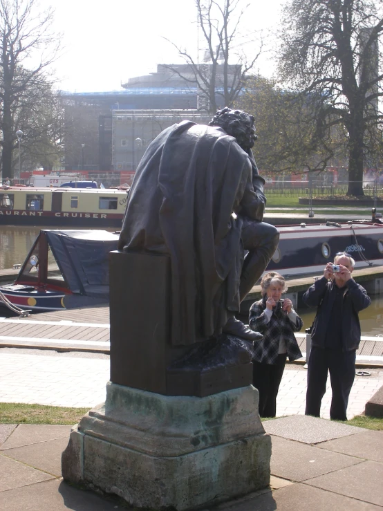 two people standing next to a statue in the park