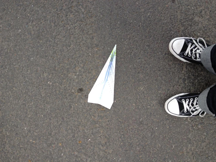 a small kite on the ground, with a person's feet standing on one