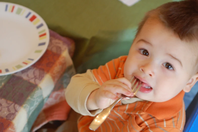 a young child brushing his teeth with a gold fork