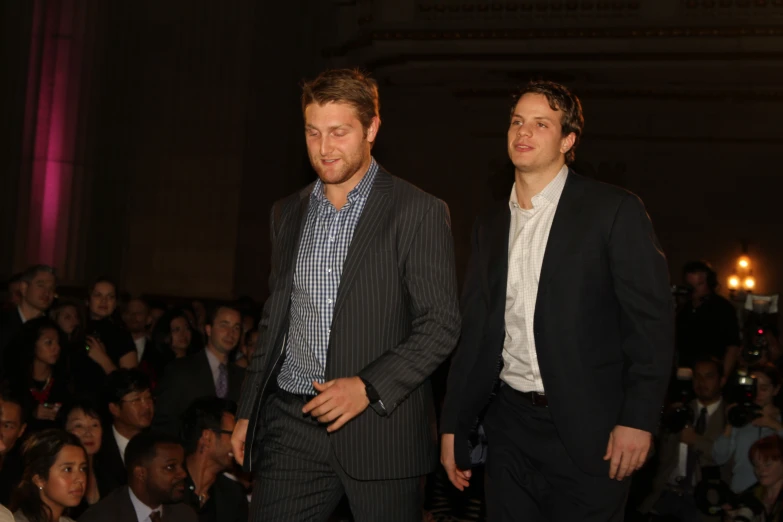 a pair of men in formal attire standing in front of a large crowd