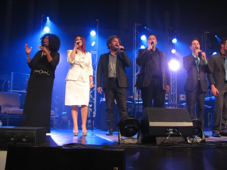 group of people on stage singing on the same microphone