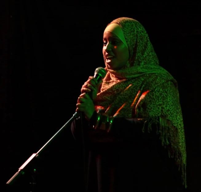 woman in hijab singing into microphone with green lights