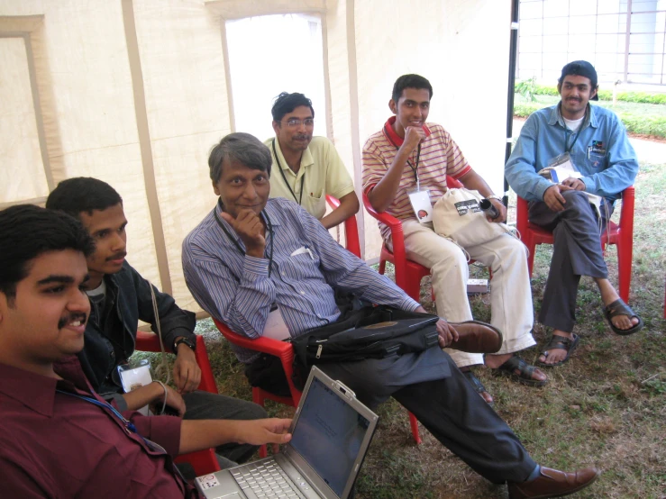 many people sitting in a small tent working on their computers