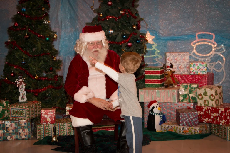a little boy looking at santa clause next to a christmas tree