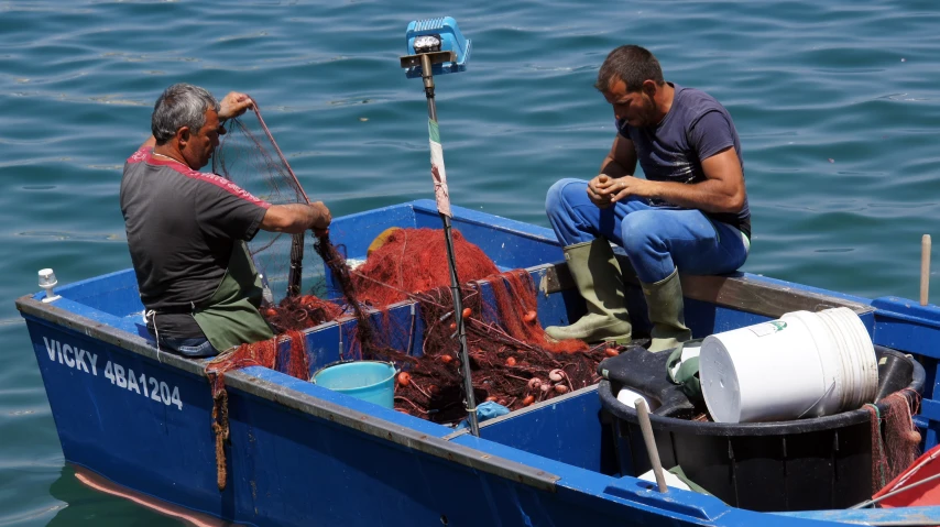 two men are in a small blue boat fishing