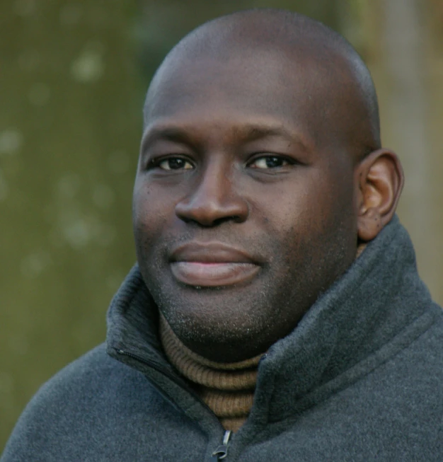 a black man with balding head and jacket looking into the distance