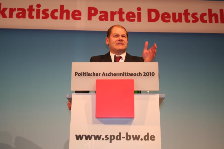 a man standing at a podium wearing a suit and tie