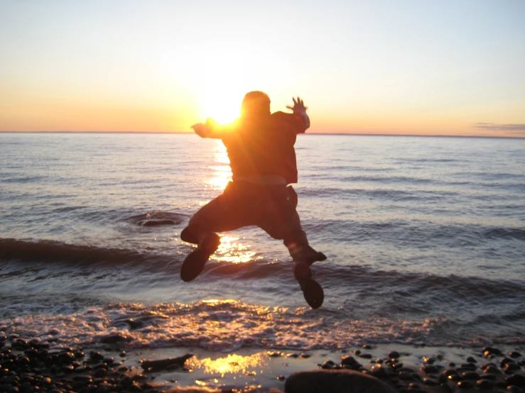 man jumping into the air on a beach at sunset