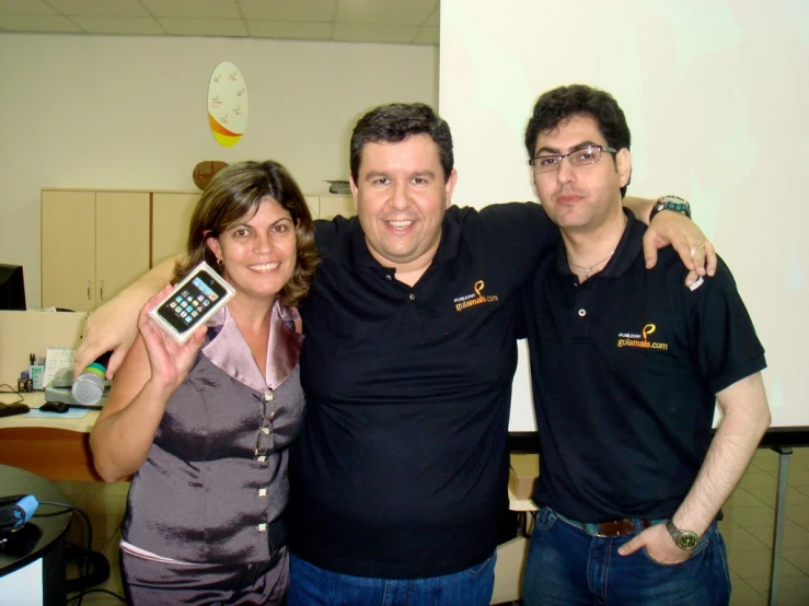 three people are standing in a room holding cell phones