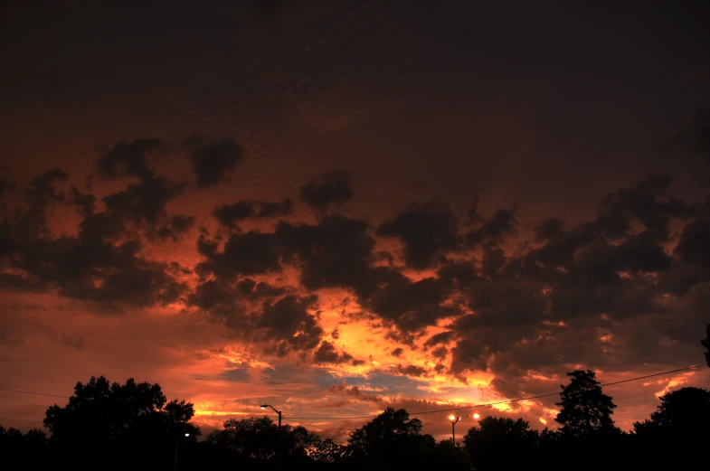 an orange sunset behind dark clouds with trees