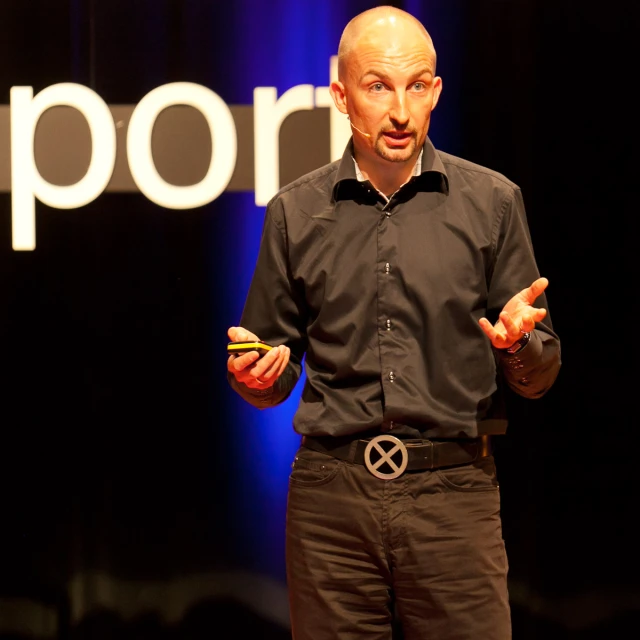 a man talking at an event with hands out