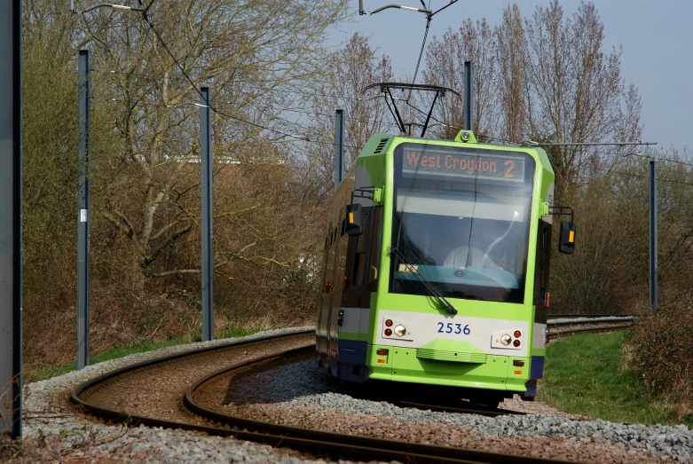 a green train traveling down tracks by some trees