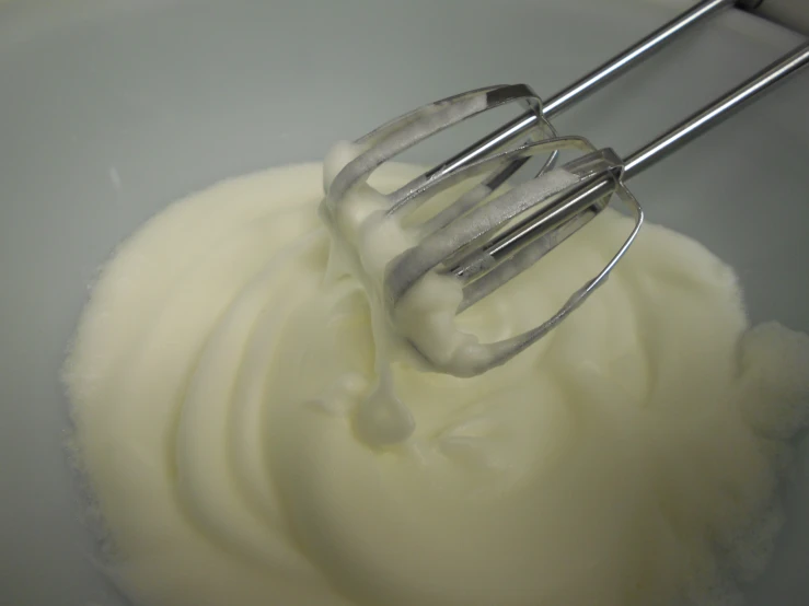 a whisk is mixing some white cream into a bowl