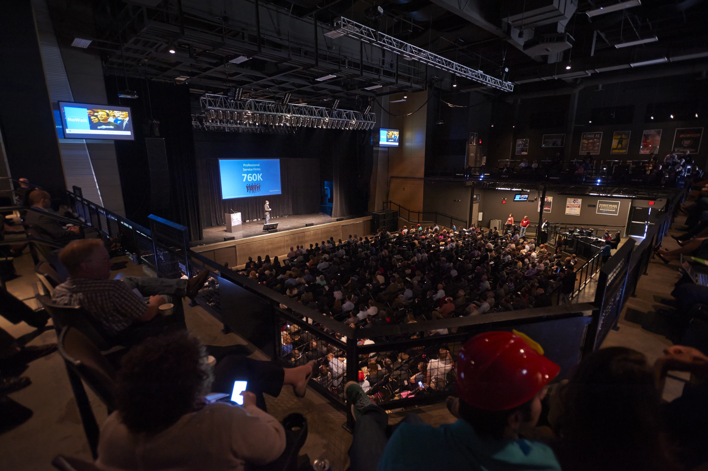 an audience in a hall with a big screen at the top of the walls