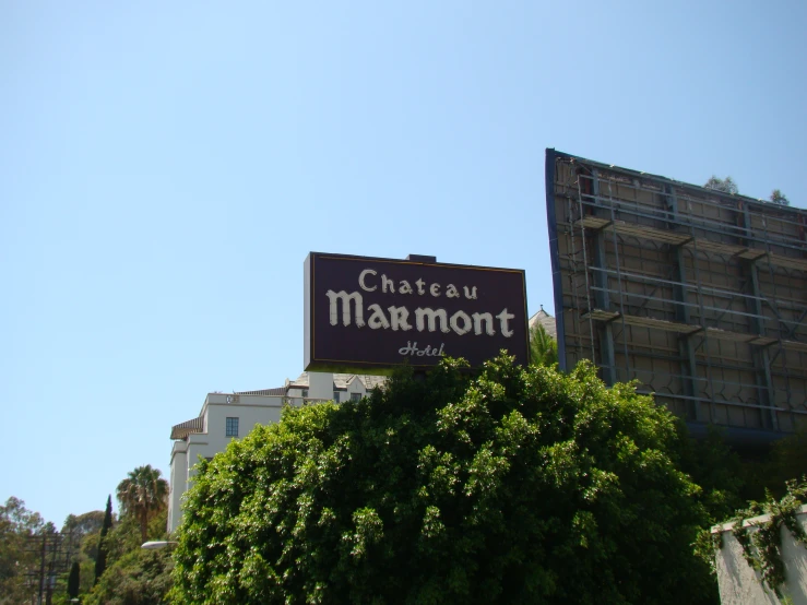 a brown sign sitting on the side of a building next to a tree