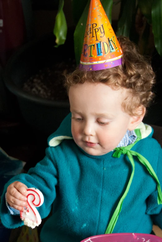 small child at a table in birthday hat and jacket looking over her plate with candy