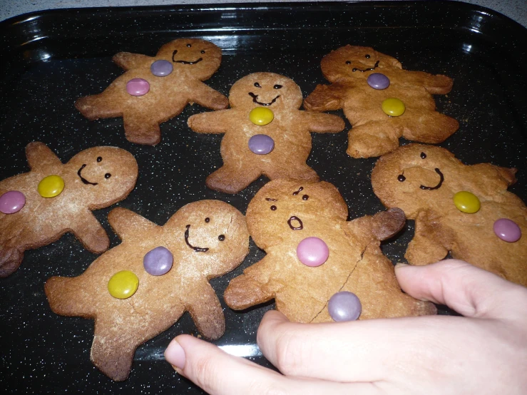 an adult hand holding over baked treats in a tray