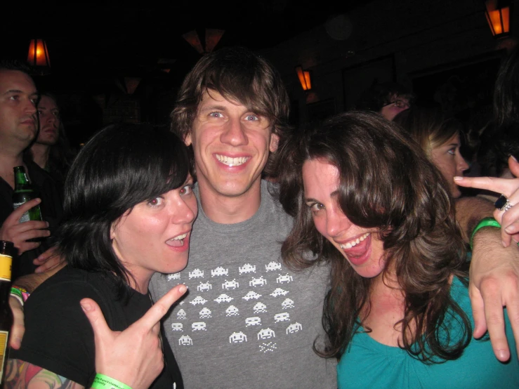 two woman and one man standing in front of the camera with their fingers in the air