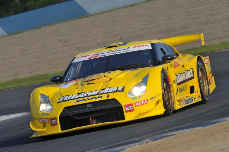 a yellow car races on a track with brown grass