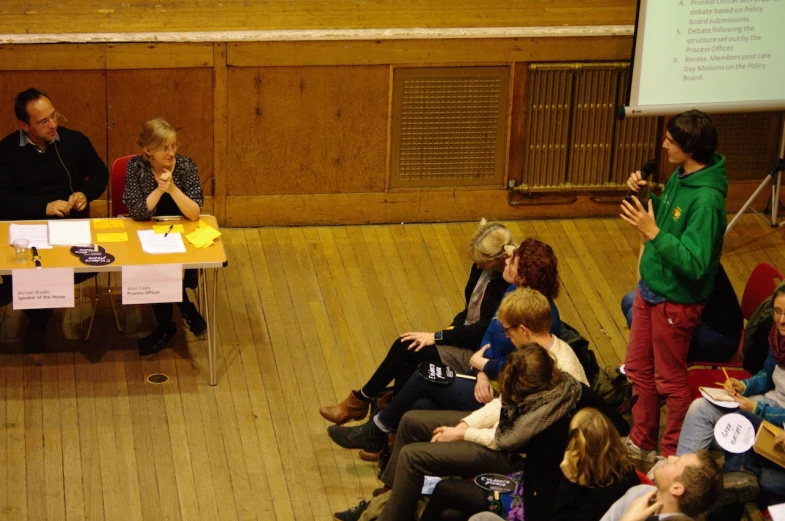 a group of people sitting around tables in front of a projector screen