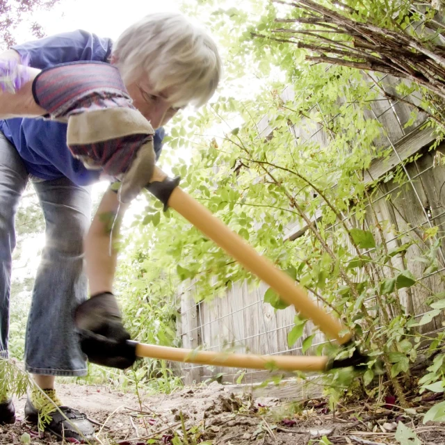 the elderly woman is cleaning up the yard with a big plastic hose