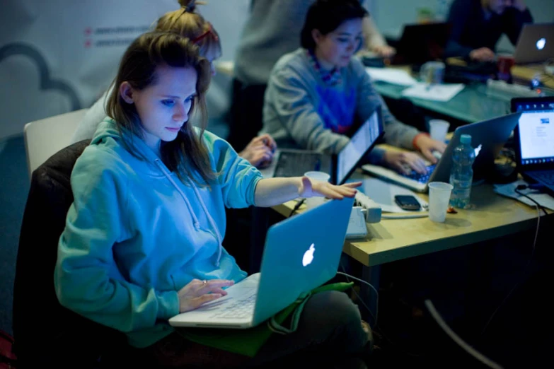 two people sit at a table with laptops